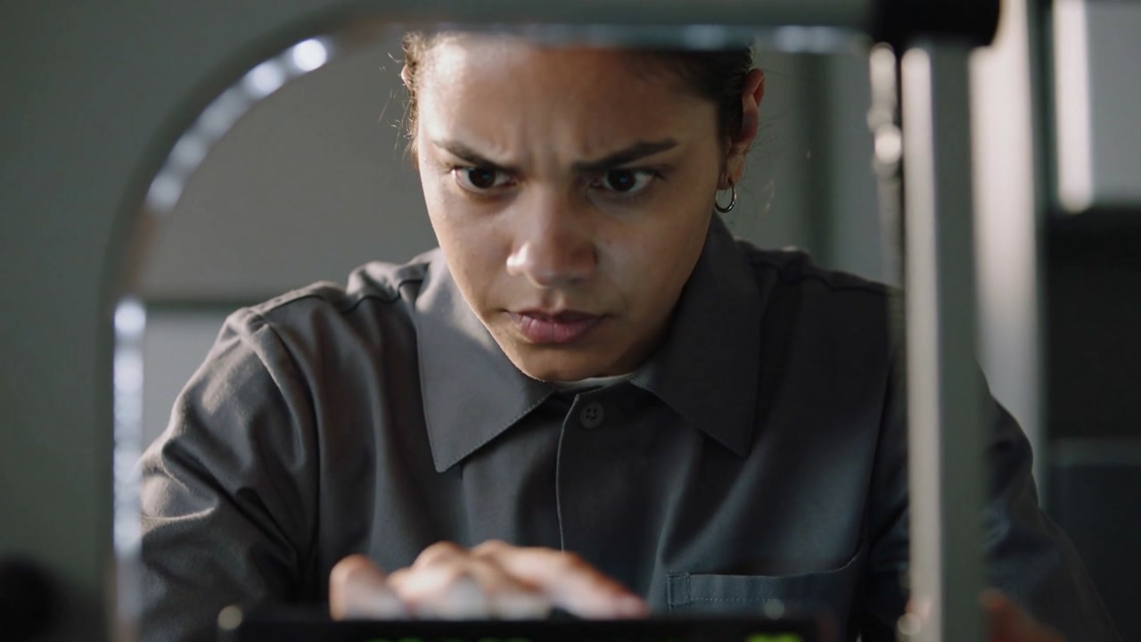 Leaning woman tech in grey shirt noticing green LED on device, adjusting buttons at lab table