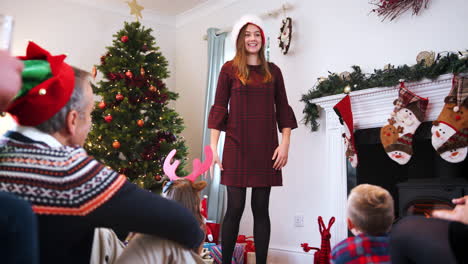 teenage girl acting out mime as multi generation family play game of christmas charades at home together