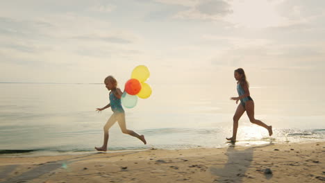 Dos-Chicas-Riendo-Juntas-Jugando-En-La-Playa,-Poniéndose-Al-Día-Sosteniendo-Globos