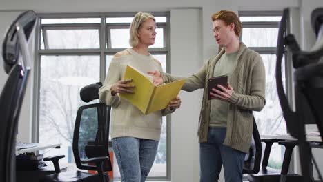 caucasian smiling male and female business colleagues discussing paperwork in office