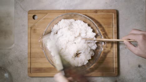 Lapso-De-Tiempo-De-Arriba-Hacia-Abajo-Del-Mostrador-De-La-Cocina-Con-Un-Tazón-De-Vidrio-De-Arroz-De-Sushi-Mezclado-Y-Enfriado-Por-Un-Ventilador-De-Mano