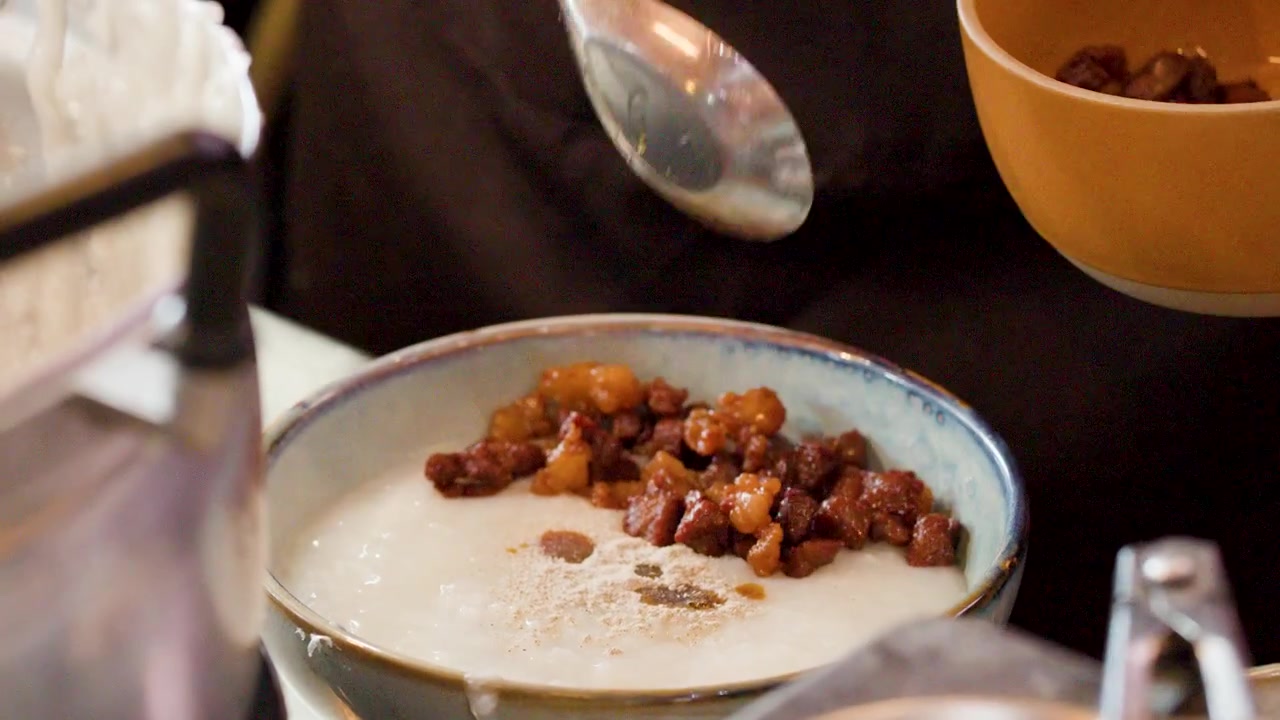 Close-up seorang koki menambahkan babi semur dan merica ke dalam mangkuk bubur.