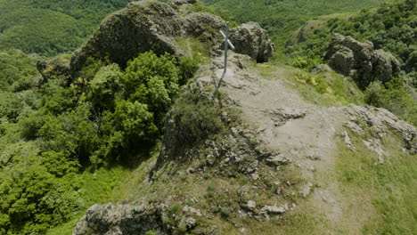 Simple-Christian-cross-on-a-rocky-hill-surrounded-with-thick,-green-bushes