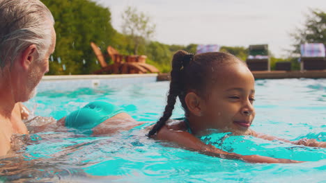 parents teaching daughter to swim on family summer holiday in pool