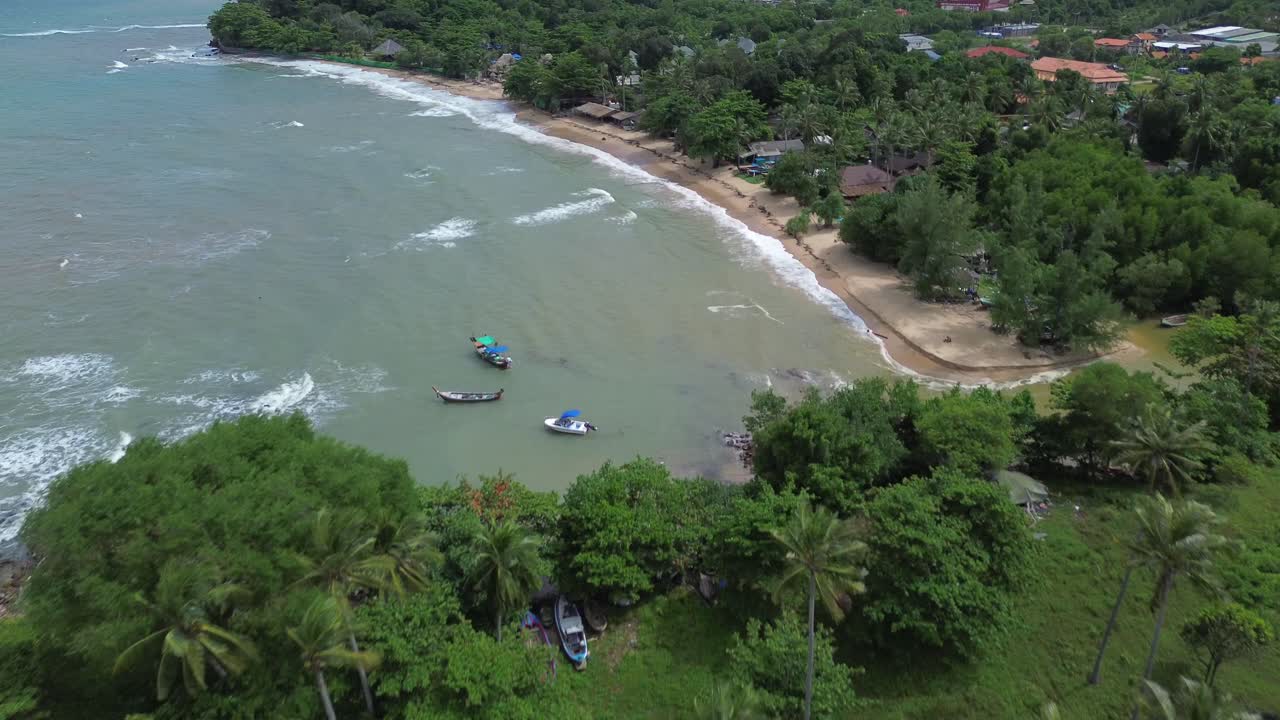 Scenic aerial footage of Koh Lanta, Thailand, showing a remote tropical coastline with lush palm trees, crystal clear turquoise water, rocky shore and hidden beaches in the distance
