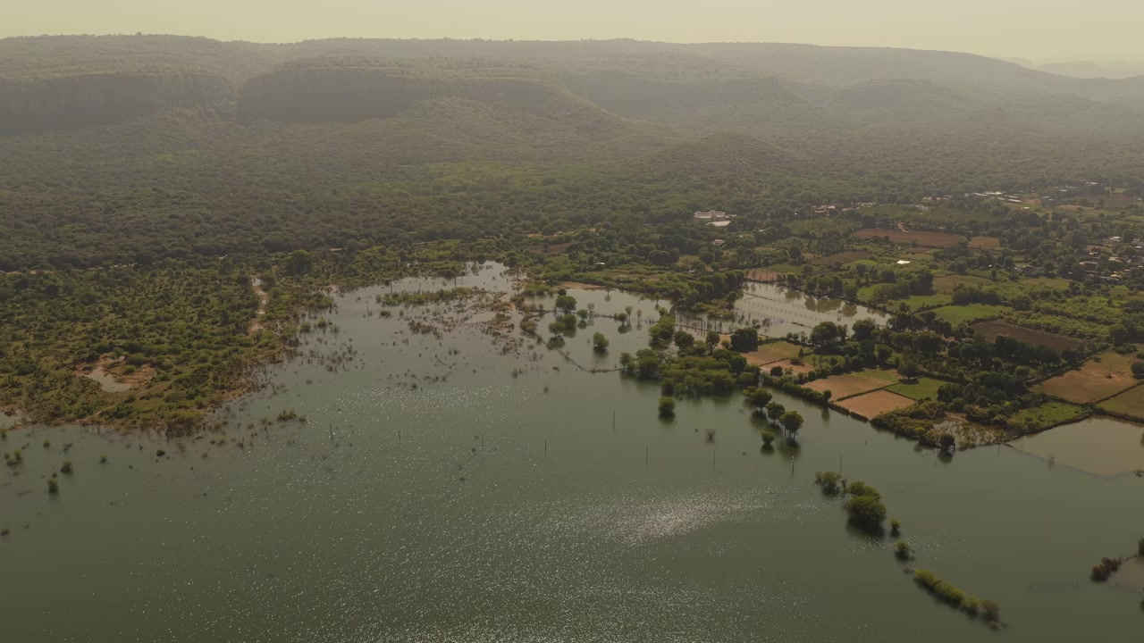 Uma ampla tomada aérea de um lago sereno cercado por campos verdes exuberantes e montanhas enevoadas na Índia. Perfeito para documentários de viagem e narrativa ambiental