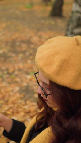 mujer pensativa con boina amarilla y silenciador lee un libro, volviendo páginas en un entorno tranquilo, rodeada de hojas doradas de otoño, disfruta de la tranquila soledad