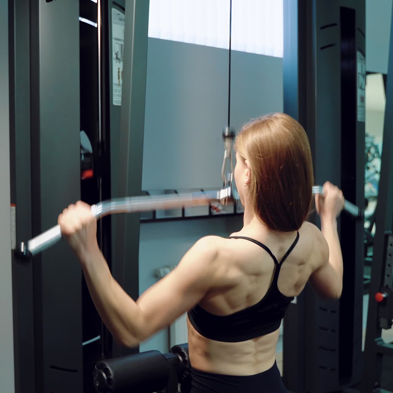 A strong woman in black top is doing vertical traction in the training in the fitness club. Close-up