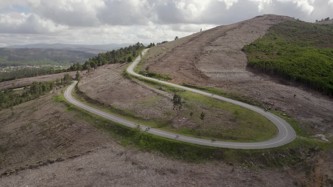 Cyclists ride a twisting mountain road carved into a stark hillside with patches of forest in northern Portugal