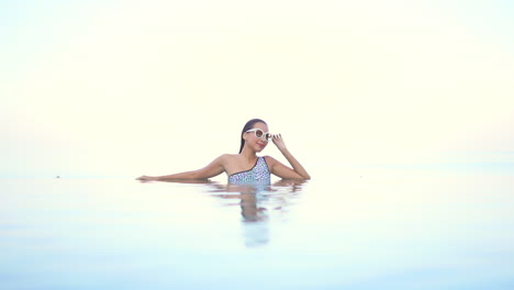 A-beautiful-woman-lounges-in-the-waters-of-a-resort's-infinity-edged-swimming-pool