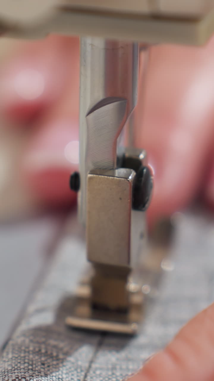 Primer plano del prensatelas de una máquina de coser sobre una tela gris tejida, manos artesanas guiando la línea de costura, luz natural suave, alineación cuidadosa y detalle a cámara lenta, ambiente acogedor de estudio en casa