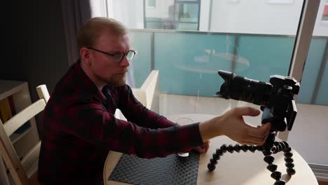 joven vlogger masculino se sienta a la mesa, ajusta la cámara para filmar, plano medio