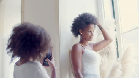 black woman posing by window while her little daughter taking photo and then showing it to mum