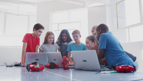 students with female teacher in after school computer coding class learning to program robot vehicle