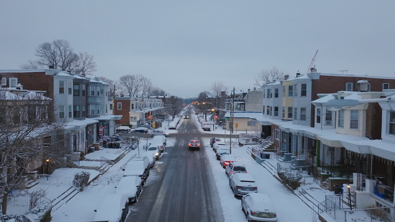 Static aerial footage of a car driving down a snow covered street in West Philadelphia, Pennsylvania.
