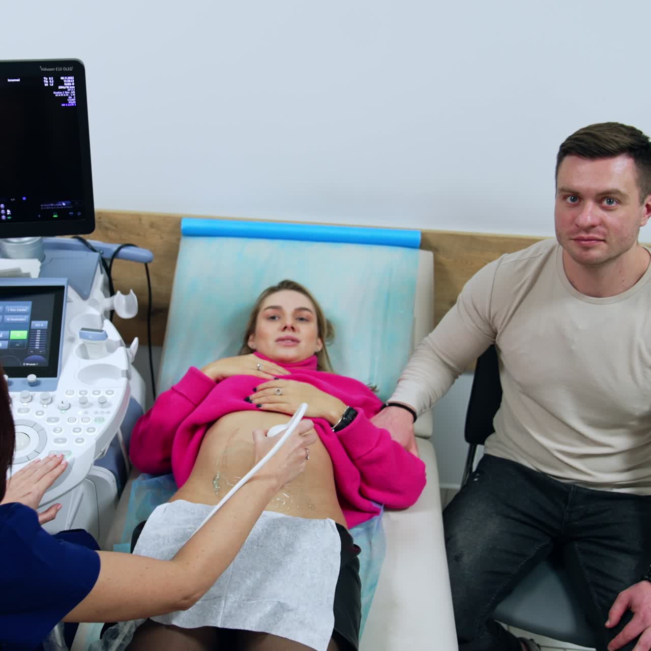 Female doctor perfroming ultrasound check for a blonde pregnant woman. Happy man supporting his wife