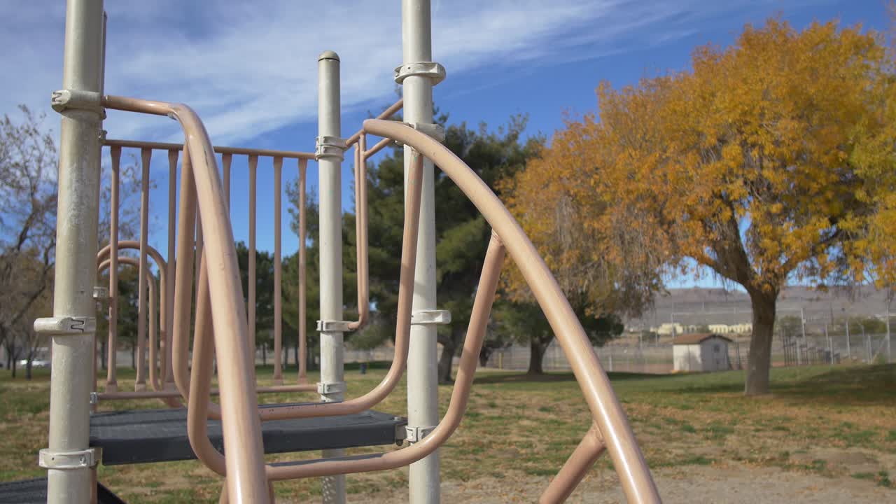 Slow pedestal down of a jungle gym next to an autumn tree with yellow leaves