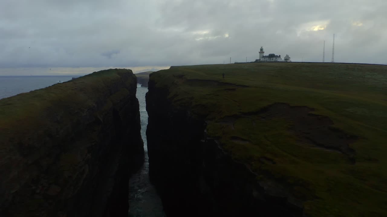 el dron se desliza entre el borde del acantilado y la pila de mar, mostrando el faro de la cabeza del bucle con el mar y el cielo a la vista