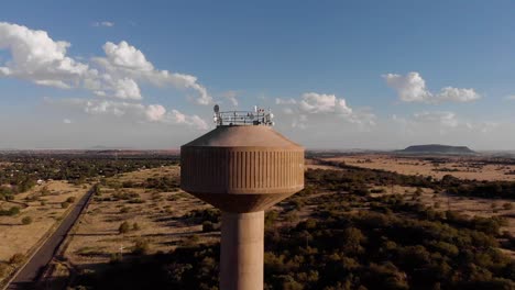 DRONE-Circling-Shot-of-a-Broadcast-Tower-in-a-Rural-Area-on-a-Sunny-Day