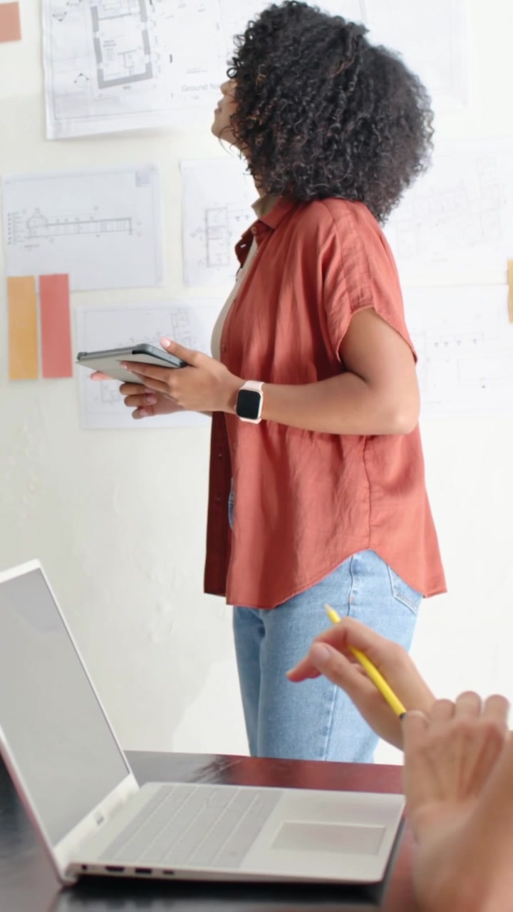 Video verticale: Inizio revisione, designer con top color ruggine che studia piani e campioni appuntati con un tablet.