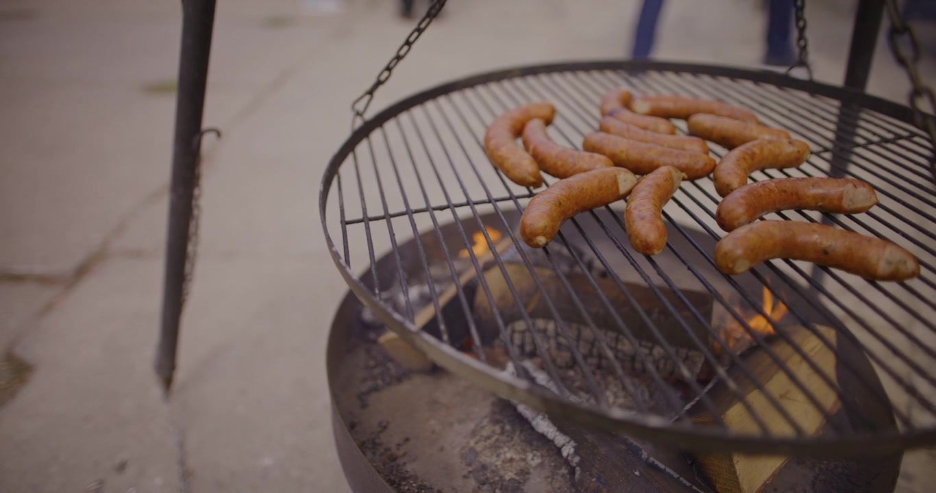 Salsicce che grigliano su un barbecue all'aperto su fuoco vivo