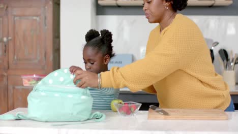 African-american-mother-and-daughter-packing-lunch-in-backpack-in-kitchen,-slow-motion
