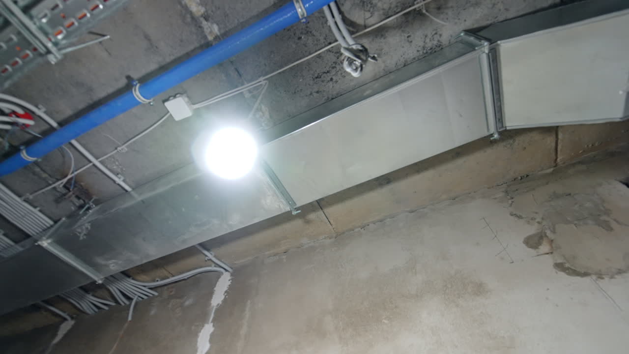 Tubi a vista nel soffitto industriale. Un ambiente industriale mostra strutture metalliche a vista, tubi blu e condotti di ventilazione contro un soffitto strutturato.