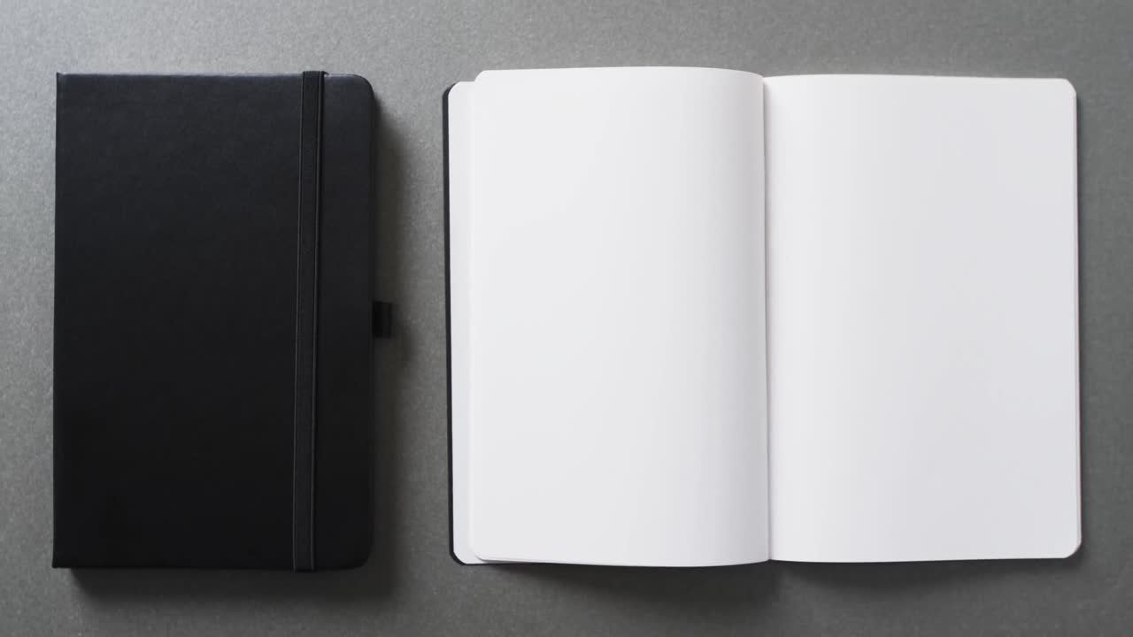 Close up of open blank book and black notebook with copy space on gray background in slow motion