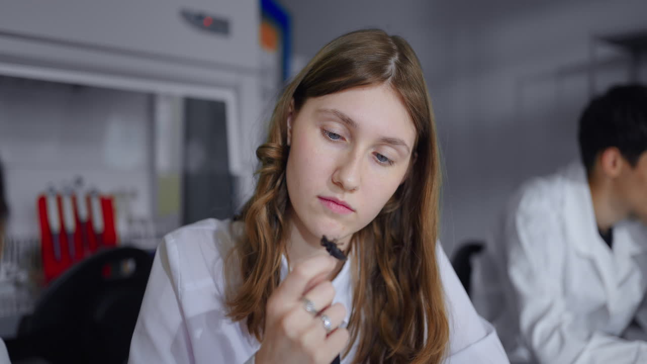 Giovane donna in camice da laboratorio che esamina un campione in un laboratorio scientifico.
