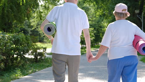 elderly couple walking hand-in-hand with yoga mats in a park
