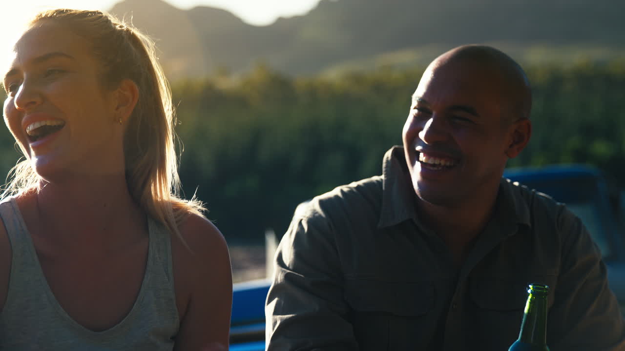 Group Of Friends By Pick Up Truck On Road Trip Drinking Beer By Lake At Sunset