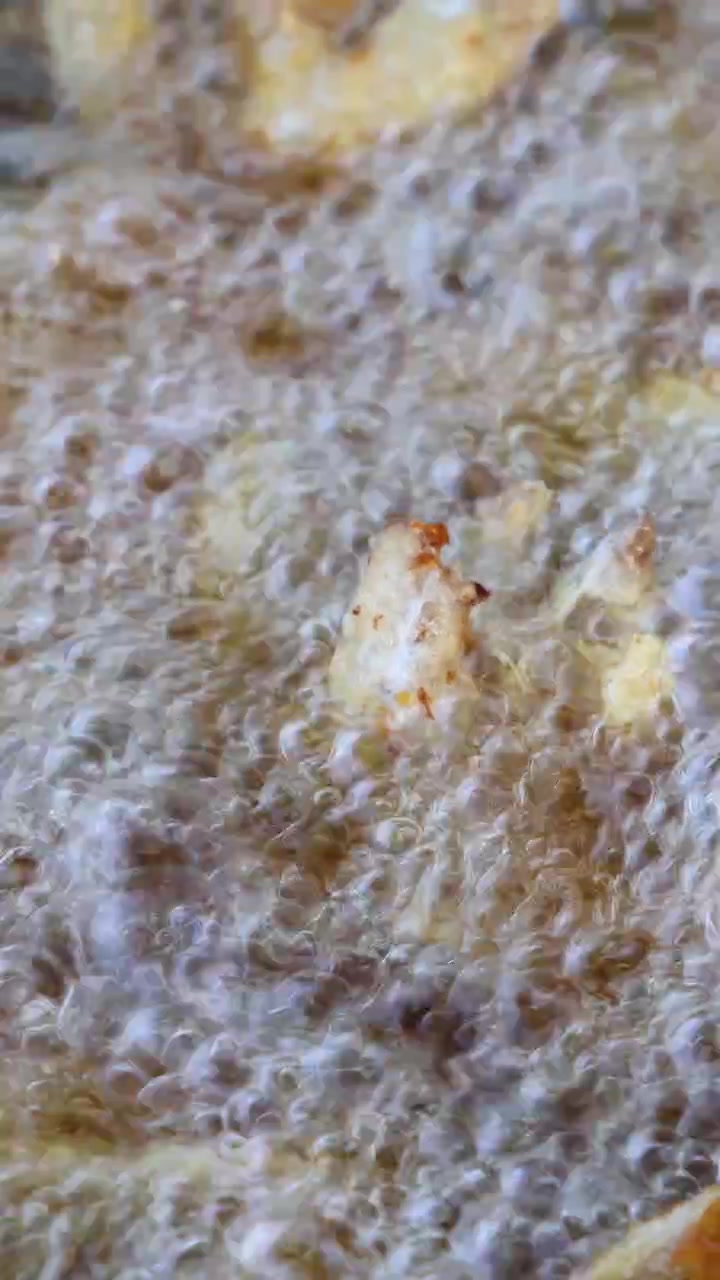 Patatine fritte dorate che friggono in olio che bolle vigorosamente, primo piano, calore elevato, illuminazione naturale, inquadratura statica
