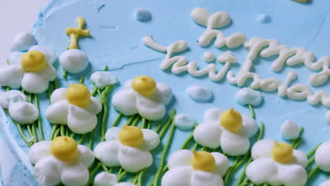 Round-cake-with-blue-colored-icing-and-a-happy-birthday-text-written-in-white-icing-and-decorative-flowers-made-of-icing