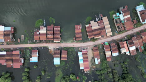 top-down aerial video of a stilt-house village divided by a narrow dirt road, with boats docked along the flooded areas