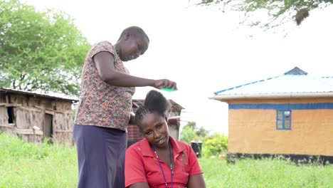 woman styling another woman's hair outdoors in a rural kenyan village setting, promoting empowerment