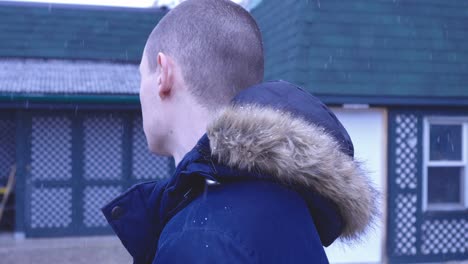 un hombre con abrigo de invierno parado afuera de su casa mientras mira alrededor con nieve cayendo en canadá - primer plano