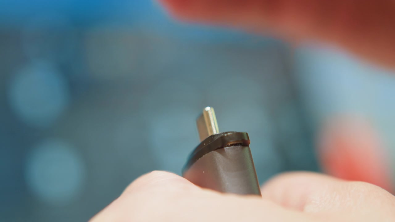 Tecnico esamina attentamente il dispositivo. Esperto ispeziona con cura il dispositivo su un tavolo da lavoro affollato. Vista dettagliata del tecnico che rimuove il coperchio ed esamina il connettore metallico con sfondo sfocato