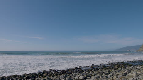 Panning-shot-of-rocky-beach-and-rolling-waves-though-the-Pacific-Ocean-located-in-Big-Sur-California