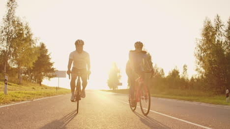two cyclists a man and a woman ride on the highway on road bikes wearing helmets and sportswear at sunset in slow motion