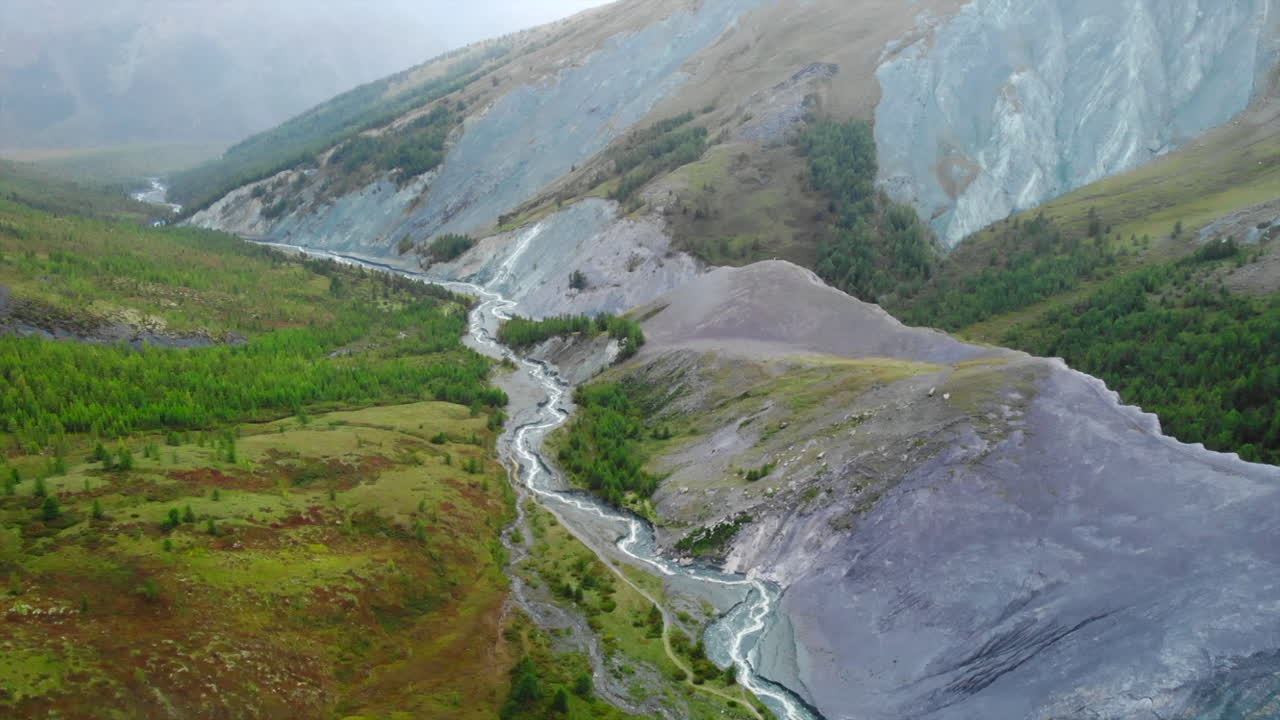 Aerial view of a winding river in a mountain valley with forests and rocky slopes