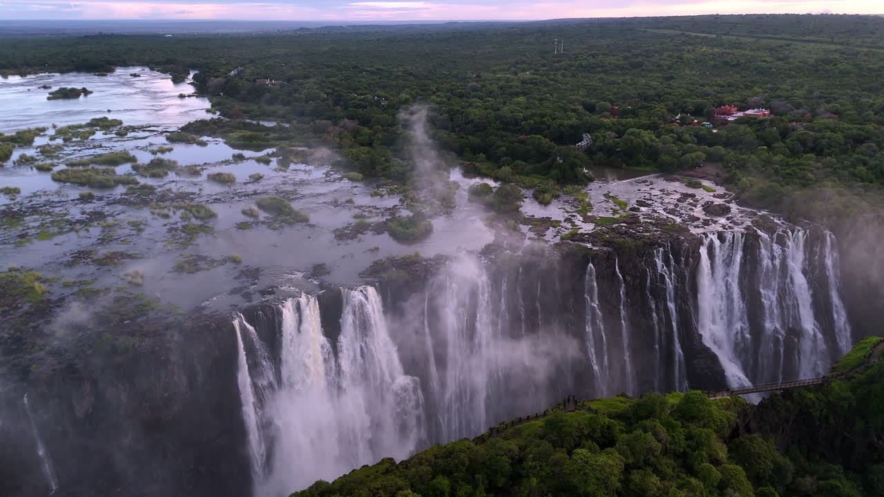 Aerial view of Victoria Falls with powerful waterfall plunging into gorge, mist rising above lush green forest, dramatic natural wonder and iconic travel destination in Africa
