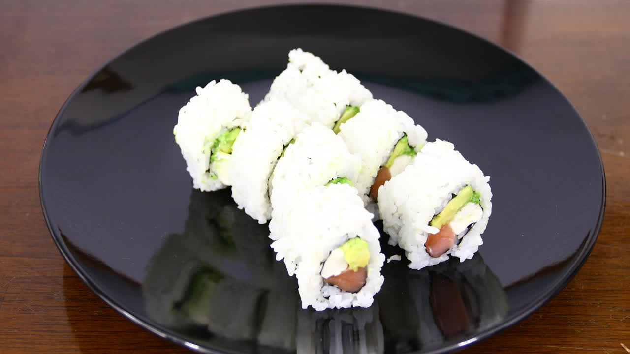 este es un video de sushi en un plato negro con una mano y palitos recogiendo un trozo