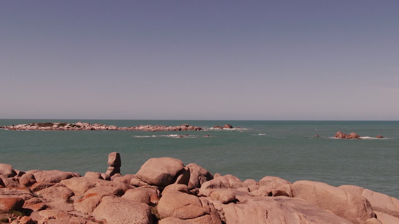 Onde calme dell'oceano si infrangono dolcemente contro una costa rocciosa sotto un cielo azzurro limpido