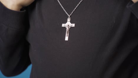 close-up christian man hangs cross necklace around his neck.