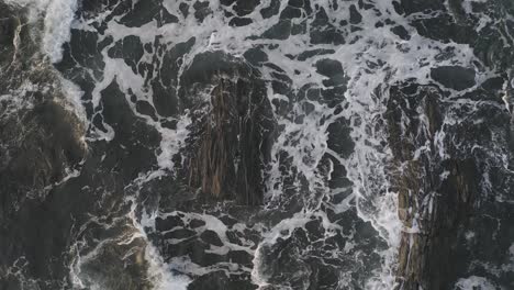 espuma marina y olas enroscadas alrededor de dos rocas expuestas al amanecer aérea de arriba hacia abajo