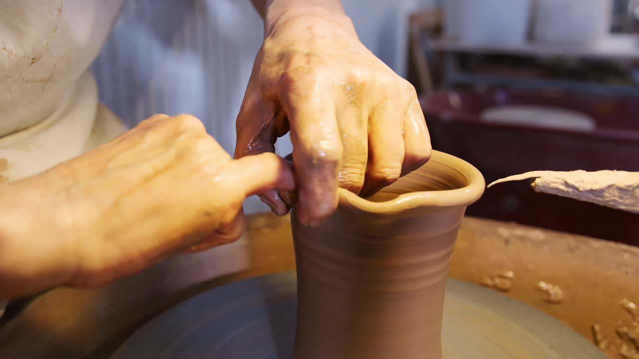 Primo piano di un vasaio che modella il collo di un vaso di argilla su un tornio in uno studio di ceramica.