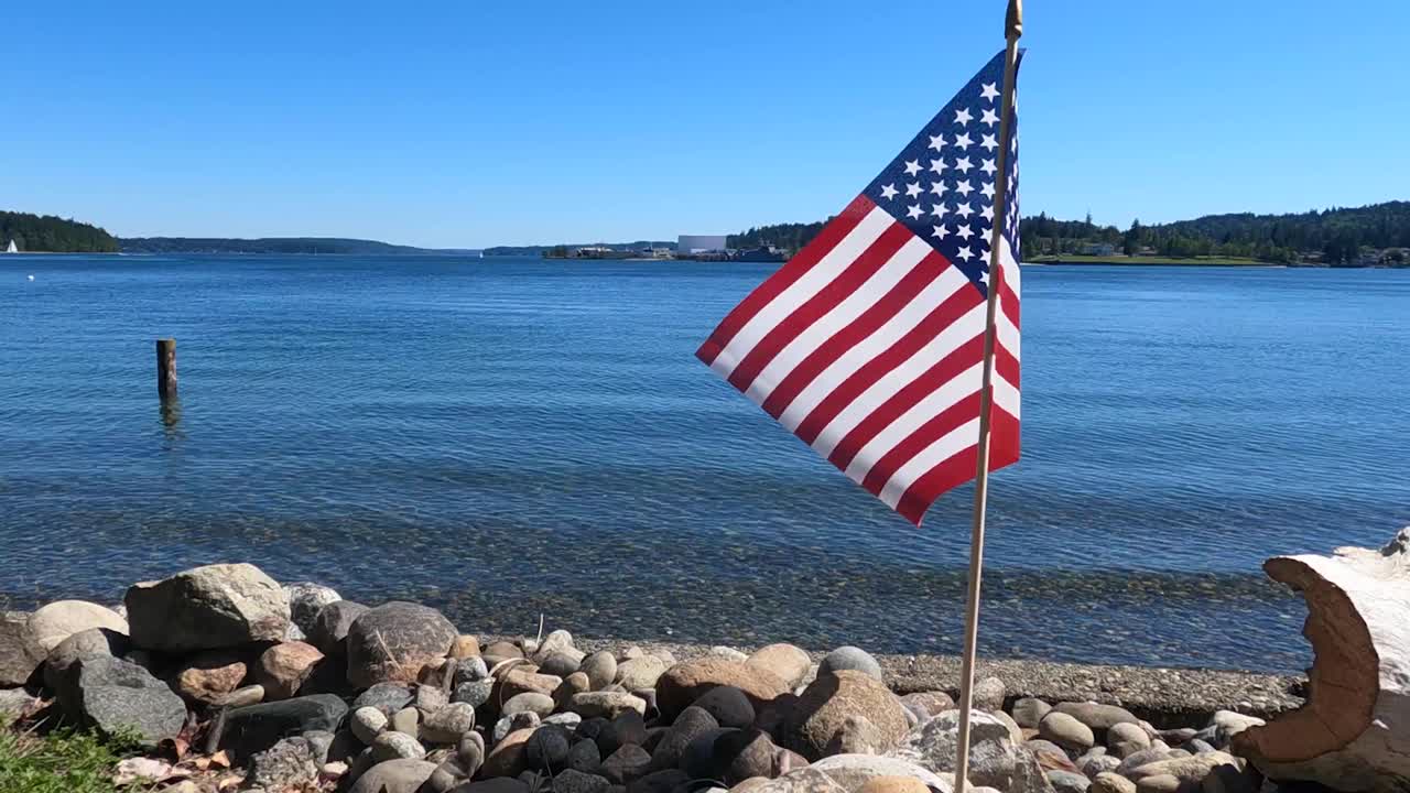 Bandiera americana con stelle e strisce che sventola al vento, ripresa dal basso, sulla spiaggia rocciosa dell'Oceano Pacifico, 4 luglio