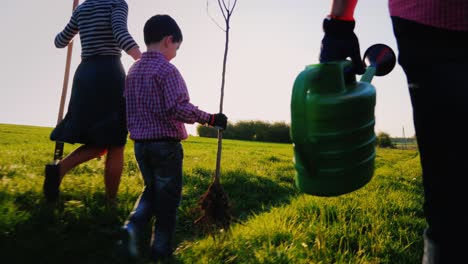 a friendly family is going to plant a tree. rear view, in the foreground of the watering can. a little boy is running around ahead. steadicam shot