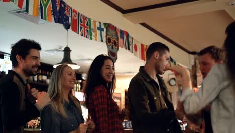 jóvenes chicas y chicos atractivos están bailando descuidadamente en un pub moderno. personas hermosas están riendo y uniéndose. bonito interior del bar y botellas con alcohol en el fondo.