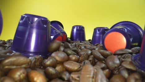 close up shot of falling roasted coffee beans between coffee capsule in front of yellow background